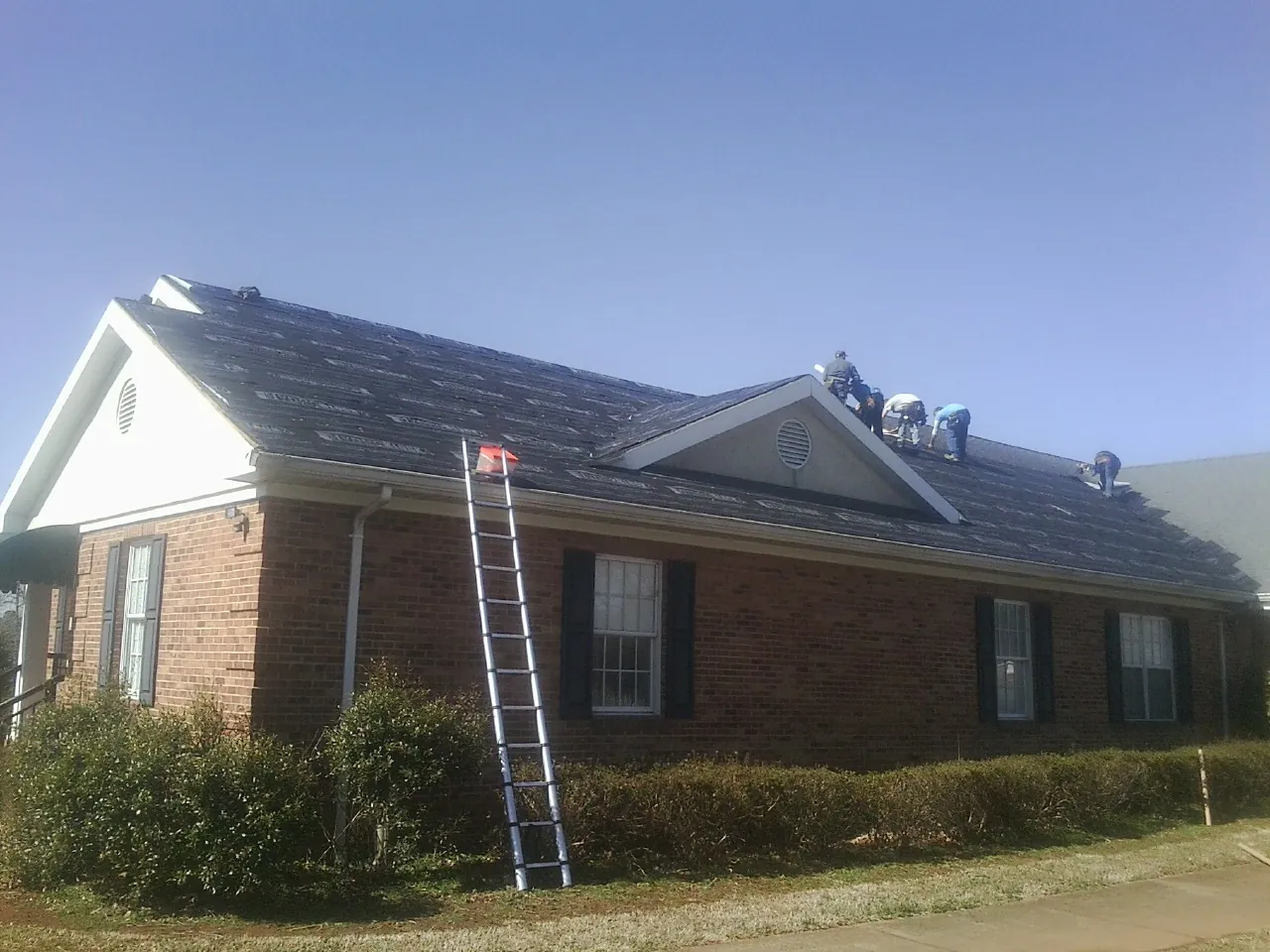 Crew tearing shingles off a brick ranch roof with a ladder set — Metal Roof Repair work by our crew in Zeigler