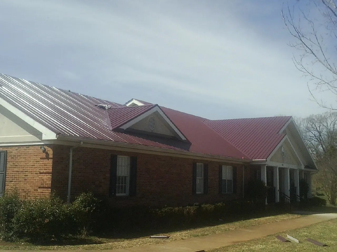 Red metal roof with gabled entries on a long brick building, from a Hail Damage Roof Repair job in Zeigler