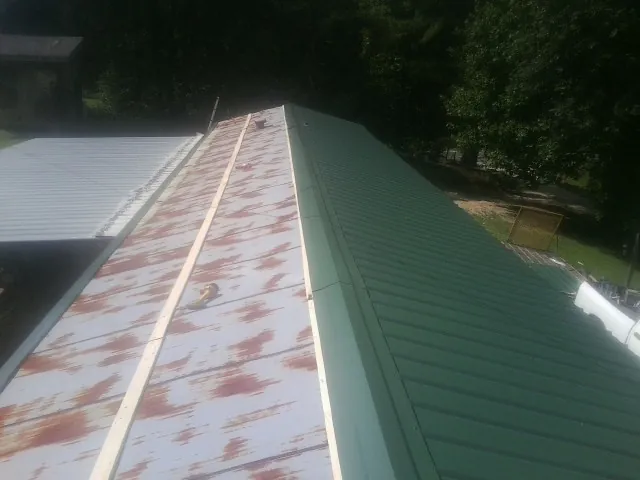 Old rusted panels beside newly installed green metal roofing in Zeigler