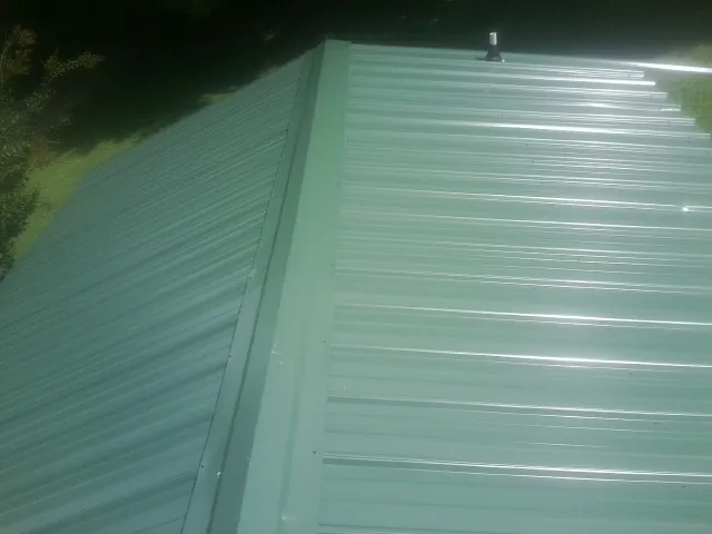 New green metal panels meeting at the ridge of a roof — Flat Roof Repair work by our crew in Zeigler