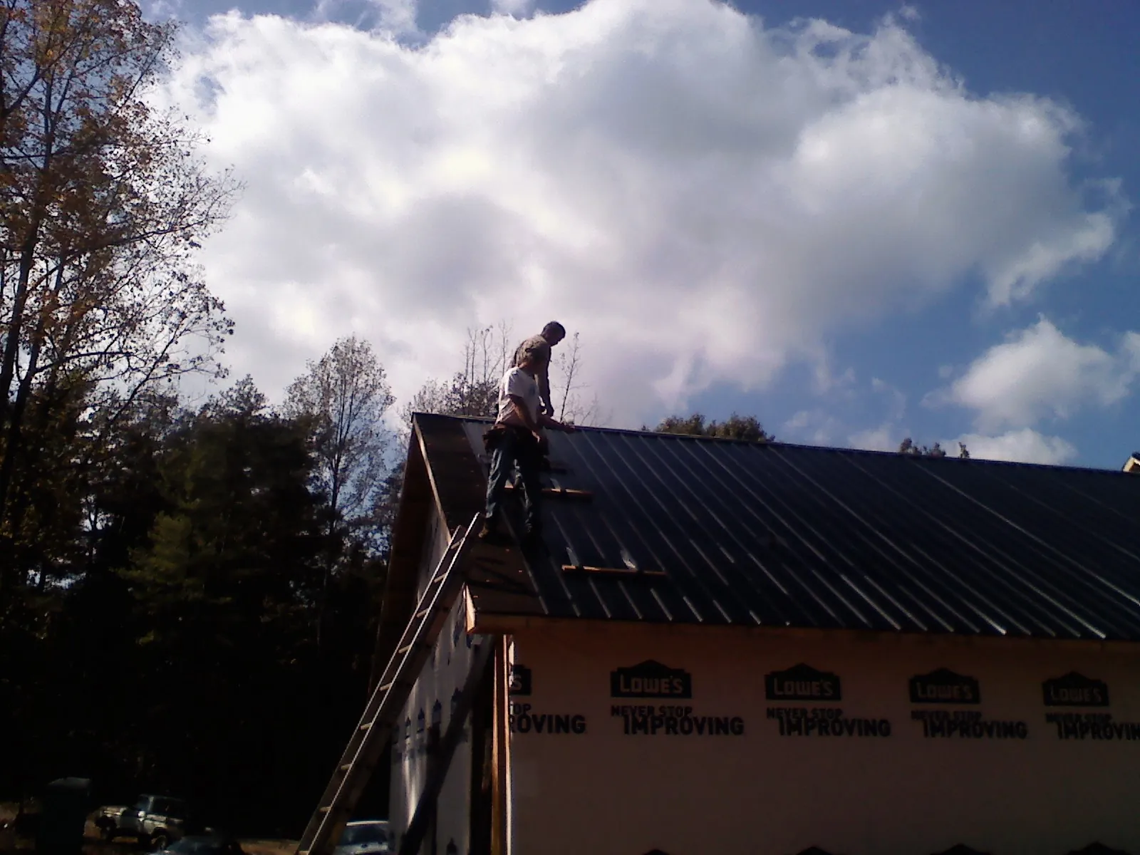 Roofer fastening dark metal panels high against a cloudy sky, from a Roof Inspection job in Zeigler